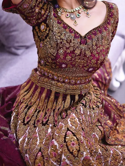 A close-up shot of a heavily embroidered maroon and gold bridal lehenga. The zardozi and velvet detailing showcase the luxurious craftsmanship that goes into my bridal wear.
