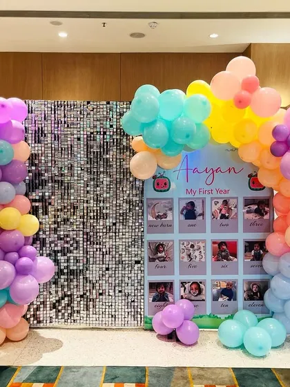 This milestone board is framed by a colorful balloon arrangement and set against a silver sequin wall, making it a standout feature of the party decor.