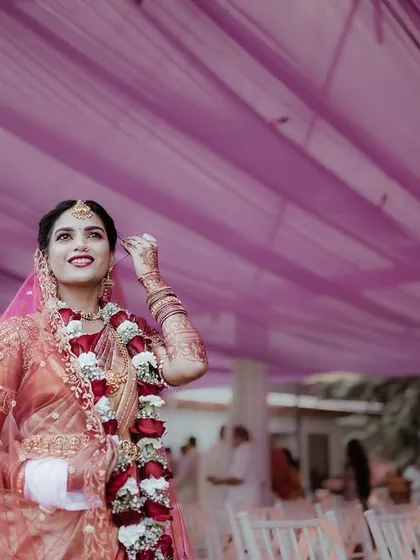 A low angle shot of the bride looking up, with the purple fabric of the mandap creating a beautiful frame. This photo highlights her joy and the festive wedding decor.