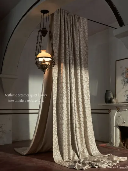 A patterned drape hangs in a room with a classic fireplace and antique lanterns. The lighting creates a sense of quiet luxury, integrating the fabric into a timeless architectural story.