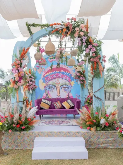 The main seating area for the couple at the carnival-themed event, featuring a custom art backdrop, pampas grass, and colorful florals.