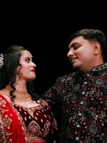 A romantic portrait of a couple at their reception, sharing a look of love. The dark background makes their ornate outfits stand out beautifully.