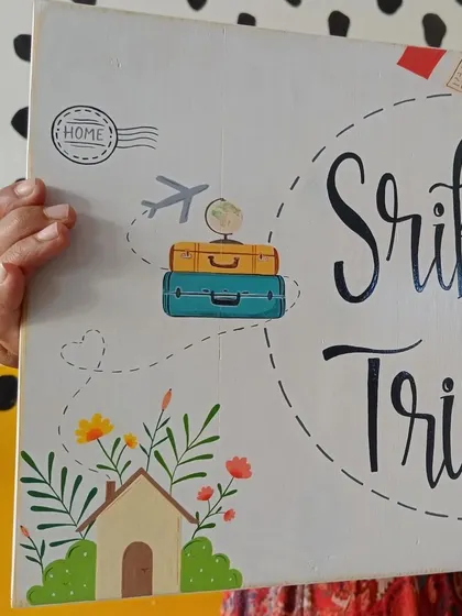 A detail shot of the "Srikant and Trisha" name board, focusing on the travel-themed illustrations that tell the story of their life together.