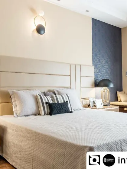 This master bedroom is a study in neutral elegance. The paneled upholstered headboard, combined with a textured blue accent wallpaper and modern light fixtures, creates a balanced and restful environment.
