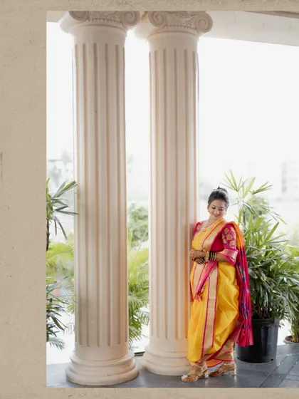 A graceful portrait of the bride in her nauvari saree, leaning against a pillar in a moment of quiet elegance.
