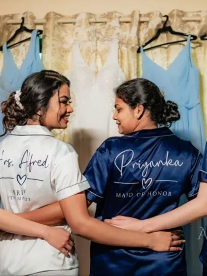 A happy moment between the bride and her maid of honor. The matching robes and hanging bridesmaids' dresses in the background show a beautifully coordinated getting-ready session.