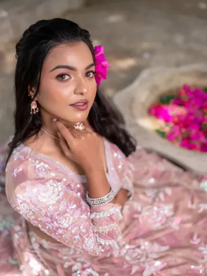 A close-up of a model's face, showing her beautiful smile and the pop of pink from the flower in her hair.