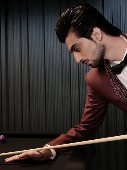 The rich color and detailed lapel of the burgundy tuxedo look striking against the dark, moody backdrop of a cocktail lounge.