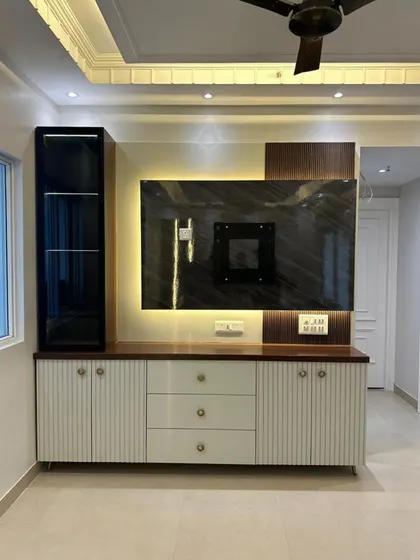 A modern entertainment center we designed, featuring a fluted white console, a dark wood-paneled display cabinet with glass doors, and a marble-finish back panel with ambient lighting for the television.