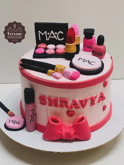 A makeup-themed cake for a beauty lover. The cake is decorated with handcrafted, edible MAC makeup products like lipstick, eyeshadow palettes, and brushes.