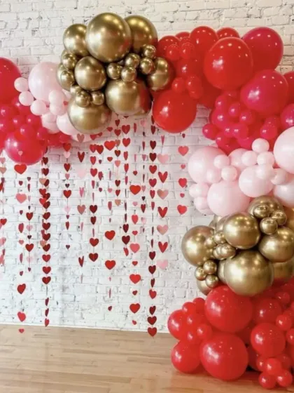 An elegant Valentine's Day or anniversary setup. This design uses a heart-string curtain with a red, pink, and gold balloon arch for a sophisticated and romantic feel.