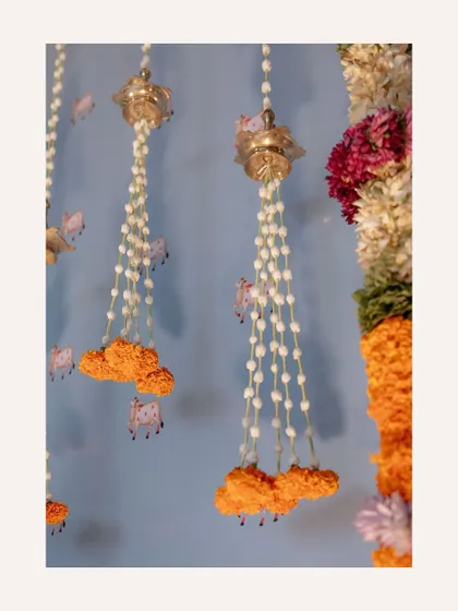 A close-up of the hanging decor, featuring jasmine strings, marigolds, and small brass bells. These delicate details add texture and a gentle sound to the ambiance.