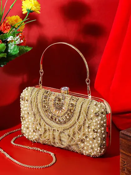 This image places a golden beaded clutch in a festive setting with a red backdrop and flowers. The composition is rich and celebratory, perfect for showcasing a party accessory.