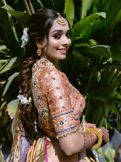 A beautiful side profile showing the intricate braid adorned with fresh flowers. The makeup is soft and romantic, a perfect match for the hairstyle.