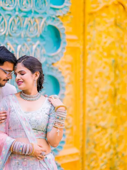 An intimate and romantic portrait of a couple in a colorful, traditional setting. The soft focus and their close embrace create a dreamy, emotional feel.