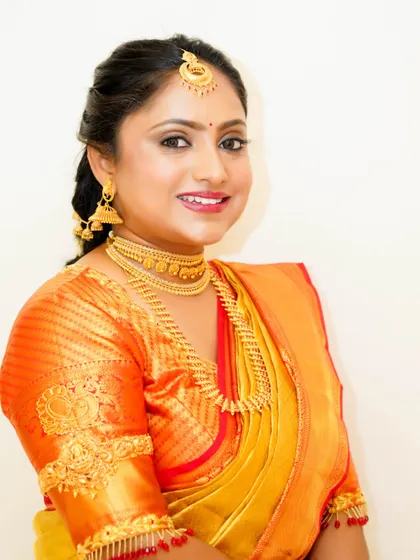 A happy bride showcasing her traditional South Indian makeup. The look features defined eyes and a bright smile, perfect for her wedding day in a vibrant orange and yellow silk saree.
