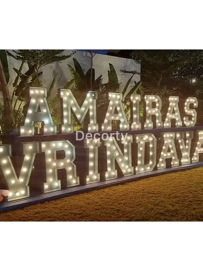 Large, illuminated marquee letters spelling out 'AMAIRAS VRINDAVAN', creating a spectacular entrance for a themed party.
