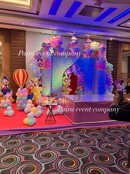 The same castle theme decoration, showing the full stage setup. The lighting enhances the colors of the castle and the pastel balloon arrangements.