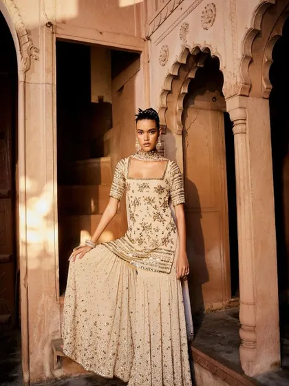 A breathtaking sharara set in a subtle beige hue. The intricate gold sequin and threadwork make this a perfect outfit for a reception or a sangeet, offering understated glamour.