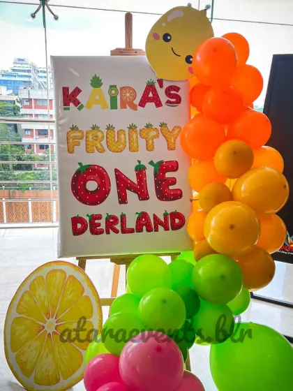 A personalized welcome easel for "Kaira's Fruity ONEderland" greets guests, framed by a vibrant balloon garland that introduces the party's cheerful color palette.