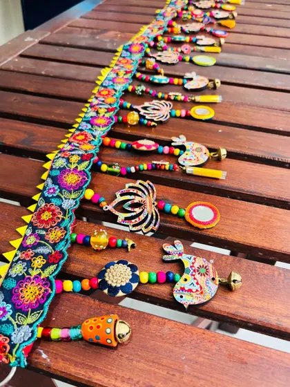 An angled view of the 'TAMAARA' toran, showcasing the layers of wooden beads, metal floral buttons, and soft tassels. Every element is hand-assembled using eco-friendly materials.