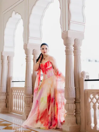 A bride in a colorful gown poses under the arches of a palace corridor, her vibrant dress a beautiful focal point in the neutral-toned architecture.