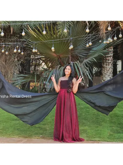 The detachable black wings on this maroon gown can be held up to create a bold, wing-like shape against the green background.