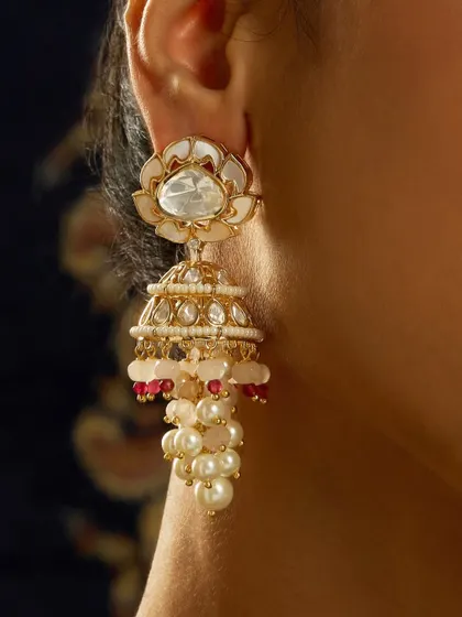 A close-up of another jhumka style, this one featuring a lotus-like motif in mother-of-pearl with pearl and ruby drops.