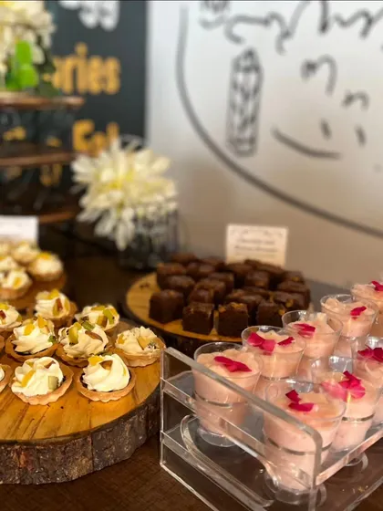 An elegant dessert spread for a corporate event, featuring mini fruit tarts, chocolate brownies, and rose-flavored mousse shots. The presentation on rustic wood slices adds a natural, sophisticated touch.