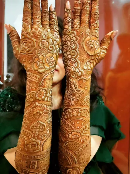 A bride peeking over her beautifully decorated hands. This is a classic pose that shows off the full glory of the bridal mehndi.