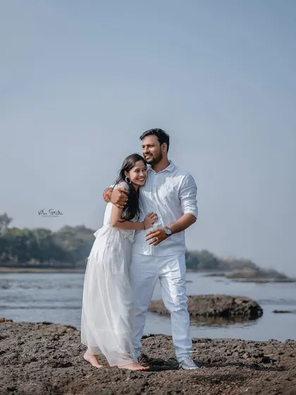 A sweet and simple embrace on the rocky shore. The couple is dressed in white, creating a clean and classic look against the natural backdrop of the river.