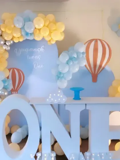 A soft and gentle hot air balloon theme for Yugansh's first birthday. The pastel yellow and blue balloon arch and "ONE" table create a light and airy feel for the celebration.