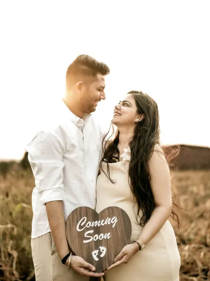 A classic portrait of the couple in a golden field, holding a "Coming Soon" sign. Their loving gaze at each other makes this a romantic and happy announcement.