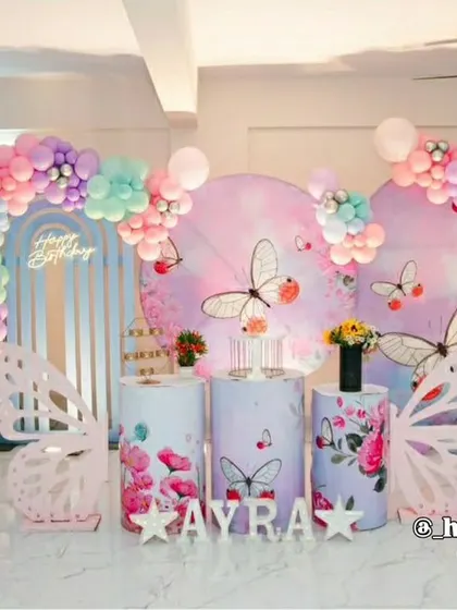 An enchanting butterfly-themed party with a pastel rainbow balloon arrangement. This setup includes large, freestanding butterfly wing props, custom-printed plinths, and a personalized backdrop, creating a magical atmosphere.