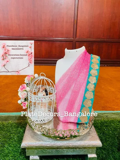 A pink and blue saree elegantly draped on a mannequin, placed on a decorative tray with a small birdcage prop. This is a creative way to gift a saree for a wedding or puberty ceremony.