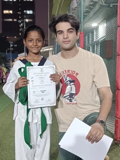 A student proudly holds her certificate and new green belt. She is a dedicated and hardworking martial artist.