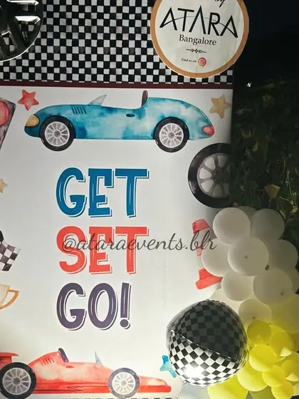 A "Get Set Go!" sign at a race car-themed party. The sign, along with checkered flag balloons, adds to the high-energy, racing atmosphere of the event.