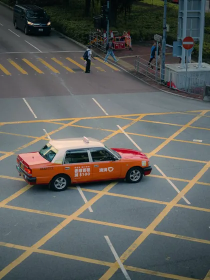 An overhead view of a red taxi on a crosshatched intersection. This perspective highlights the graphic and geometric patterns of the city streets.