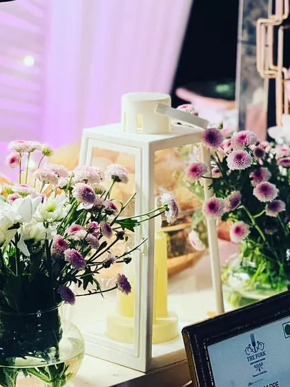 Close-up of a buffet station highlighting the small details that make a difference. Fresh floral arrangements, ambient lanterns, and neatly stacked plates contribute to a welcoming and well-organized guest experience.