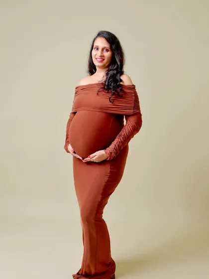 A classic, full-length portrait in a form-fitting brown dress. The clean, solid background and simple pose create a timeless and elegant look.