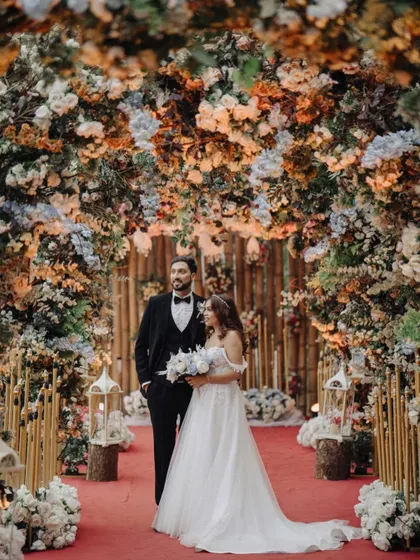 A grand portrait of the couple standing under a magnificent floral arch. This image showcases the beautiful decor and the elegance of the bride and groom.
