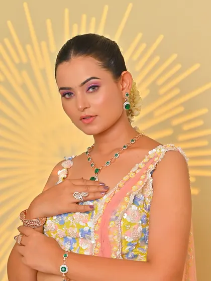 A modern Haldi look with a pastel lehenga and emerald jewelry. The makeup is soft and glowing, with a pop of color on the eyes.