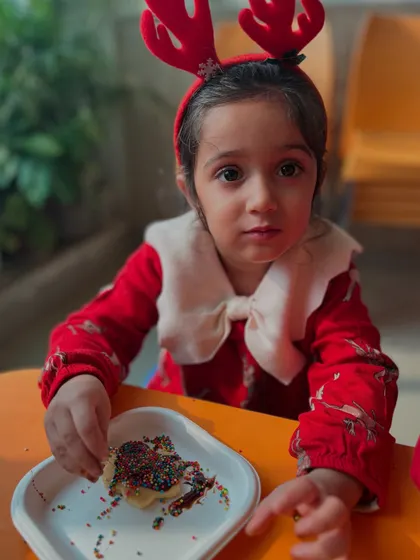 A child wearing reindeer antlers enjoys a cookie she decorated herself.