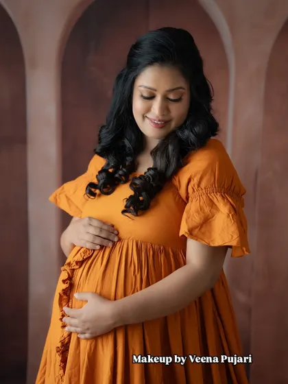 A modern maternity look. This mom-to-be looks radiant and comfortable in a beautiful orange dress, with soft curls and natural makeup.