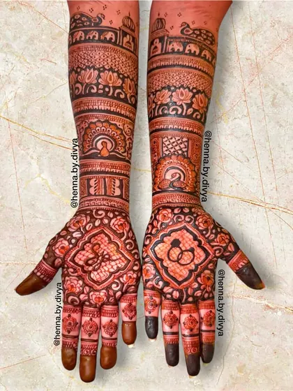 An intricate engagement mehendi extending up the arms. The palms feature the initials 'JB' and an engagement ring symbol, while the arms have detailed traditional patterns.