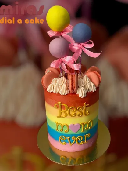 A colorful rainbow cake for the "Best Mom Ever." Topped with macarons and a balloon cluster, this vibrant cake is a joyful tribute to an amazing mom.