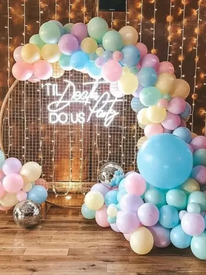 A fun and colorful balloon backdrop for a party. The pastel rainbow balloon arch, "Til Death Do Us Party" neon sign, and disco balls create a playful and festive photo opportunity.