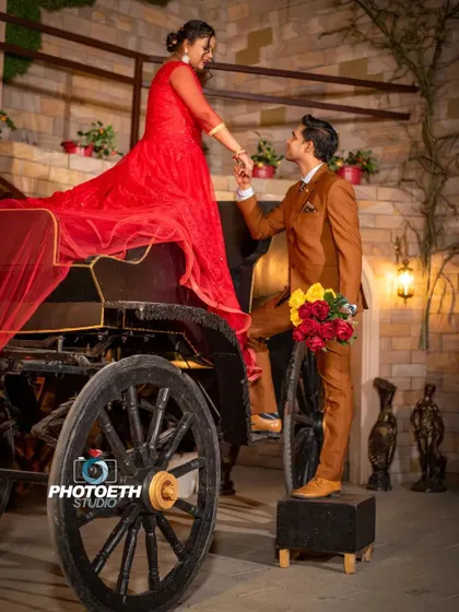 A classic fairytale moment. The groom helps his bride, dressed in a beautiful red gown, out of a vintage carriage, creating a timeless and romantic image.