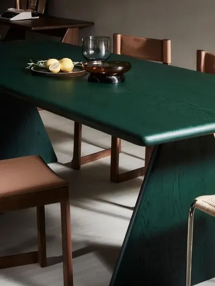 The Conica Dining Table in dark green, surrounded by Tan Side Chairs. The contrast between the table's bold, modern form and the chairs' warm walnut and leather creates a dining space that is both sophisticated and inviting.