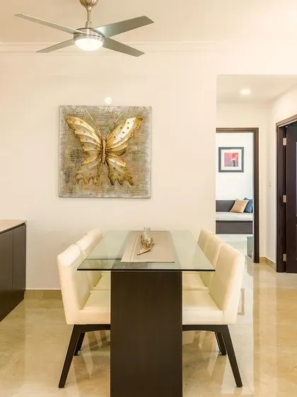 This minimalist dining area feels warm and inviting. Natural light, soft neutral colors, and modern furniture create a calming atmosphere, with a striking gold butterfly artwork adding a touch of elegance.